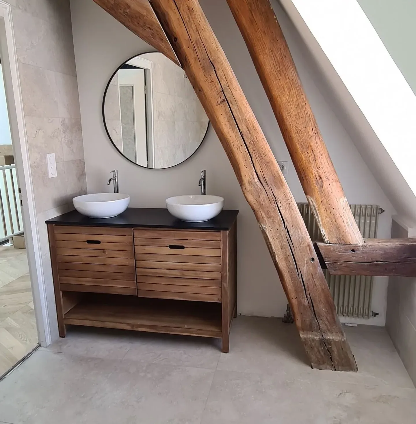 Salle de bains avec poutres apparentes, double vasque, miroir rond et meuble-lavabo en bois. — Plombier — par Au fil de l'eau — à Orgeux